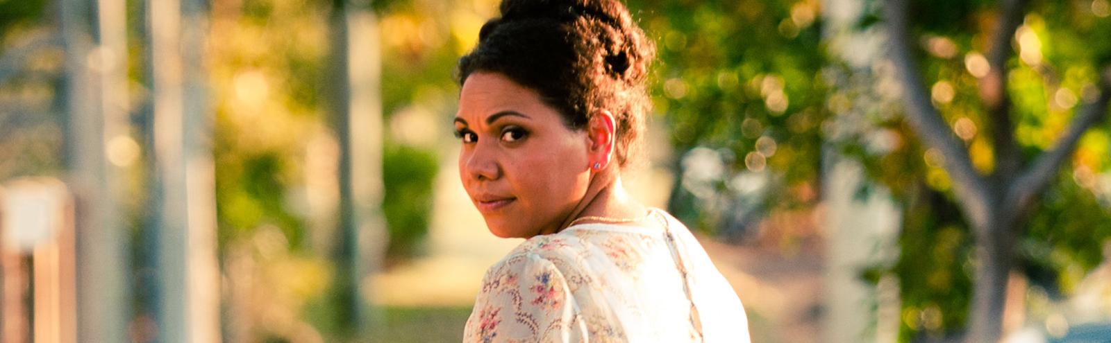 Actor Deborah Mailman in a floral dress with her back to camera and her head turned to look back over her shoulder.