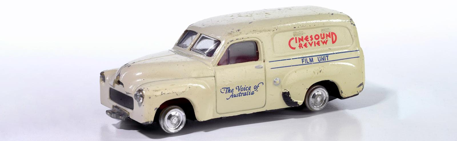 A scaled down model of a cream coloured FJ Holden panel van with the words 'Cinesound Review' and 'The Voice of Australia' painted on the side.