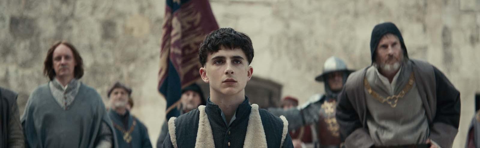 Timothee Chalamet as Henry V, surrounded by courtiers in a scene from the movie The King
