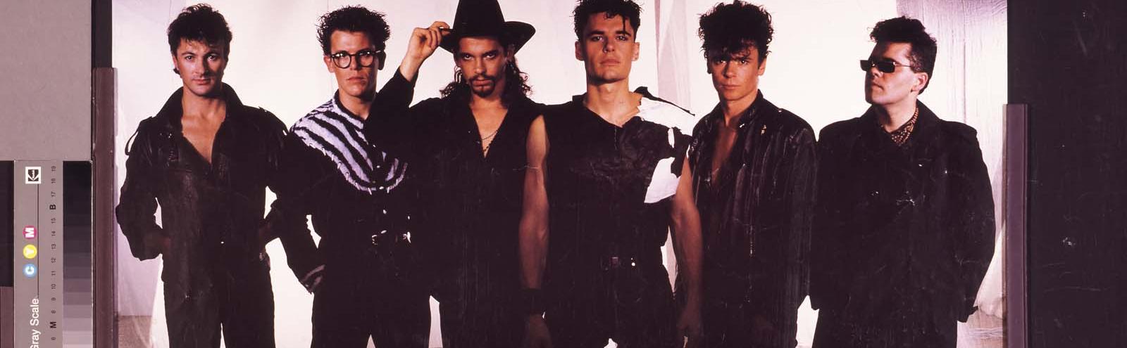 The band members of INXS pose for a studio publicity shot in the late 1980s. Lead singer Michael Hutchence has a beard and is wearing a black cowboy hat