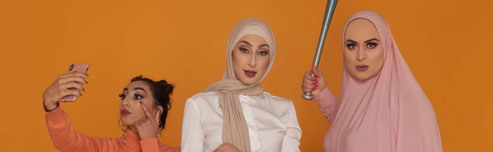 Three women standing in a row looking at camera. One is looking into her phone and the other two are looking into the camera. One is holding a baseball bat and looking angry.