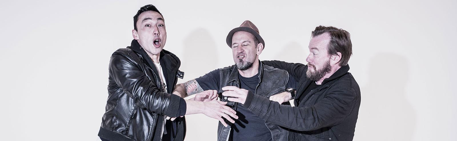 Three band members from Regurgitator comically pushing and shoving each other. 