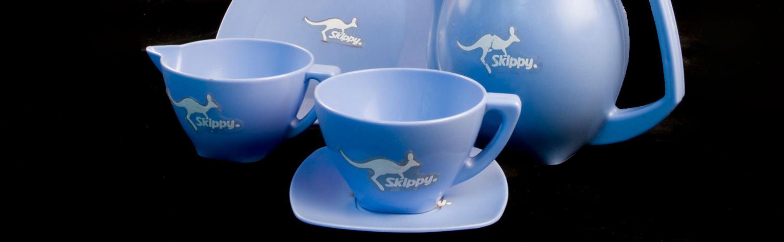 A blue plastic tea set embossed with the Skippy TV series logo and a kangaroo and consisting of tea cup and saucer, milk jug and plates