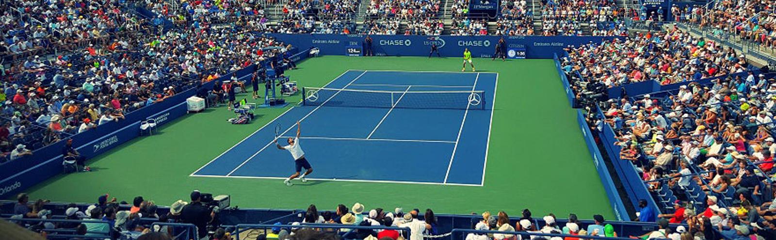 A competitive tennis match in progress watched on all sides by stands filled with seated spectators