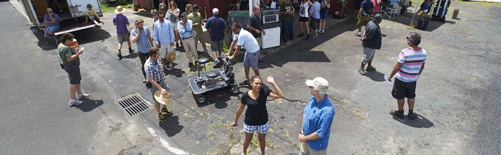 Looking down on the set of the TV series The Gods of Wheat Street. A small crowd of crew members are standing outside the set of a petrol station. 