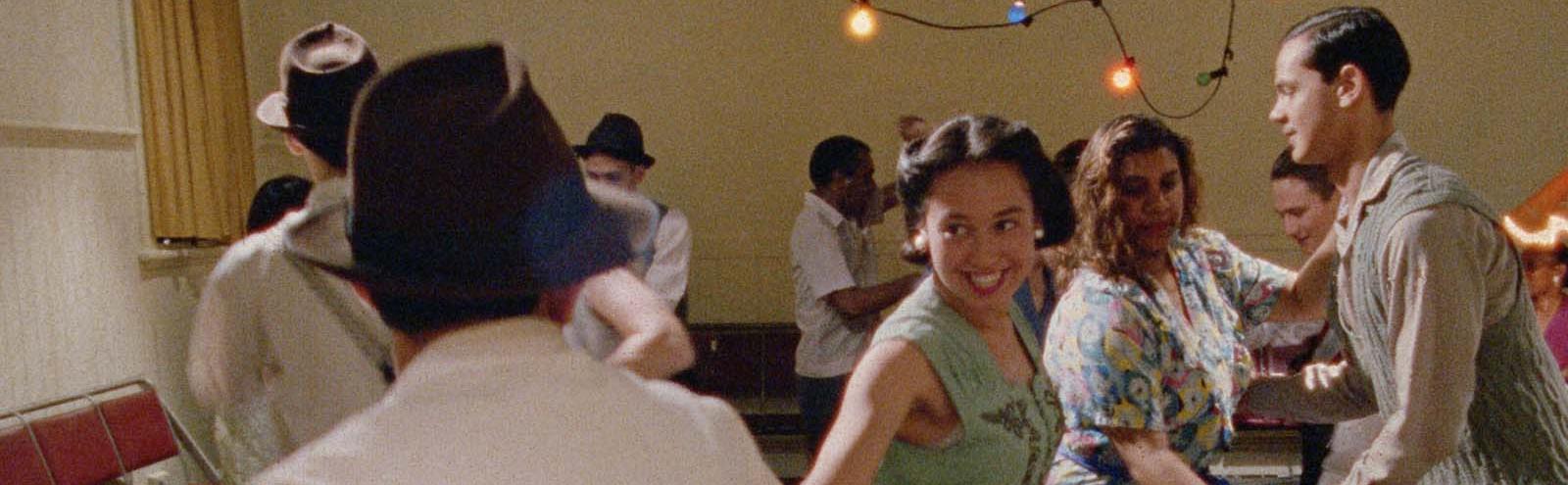 A mix of white and First Nations people dressed in 1950s clothes dancing together. 