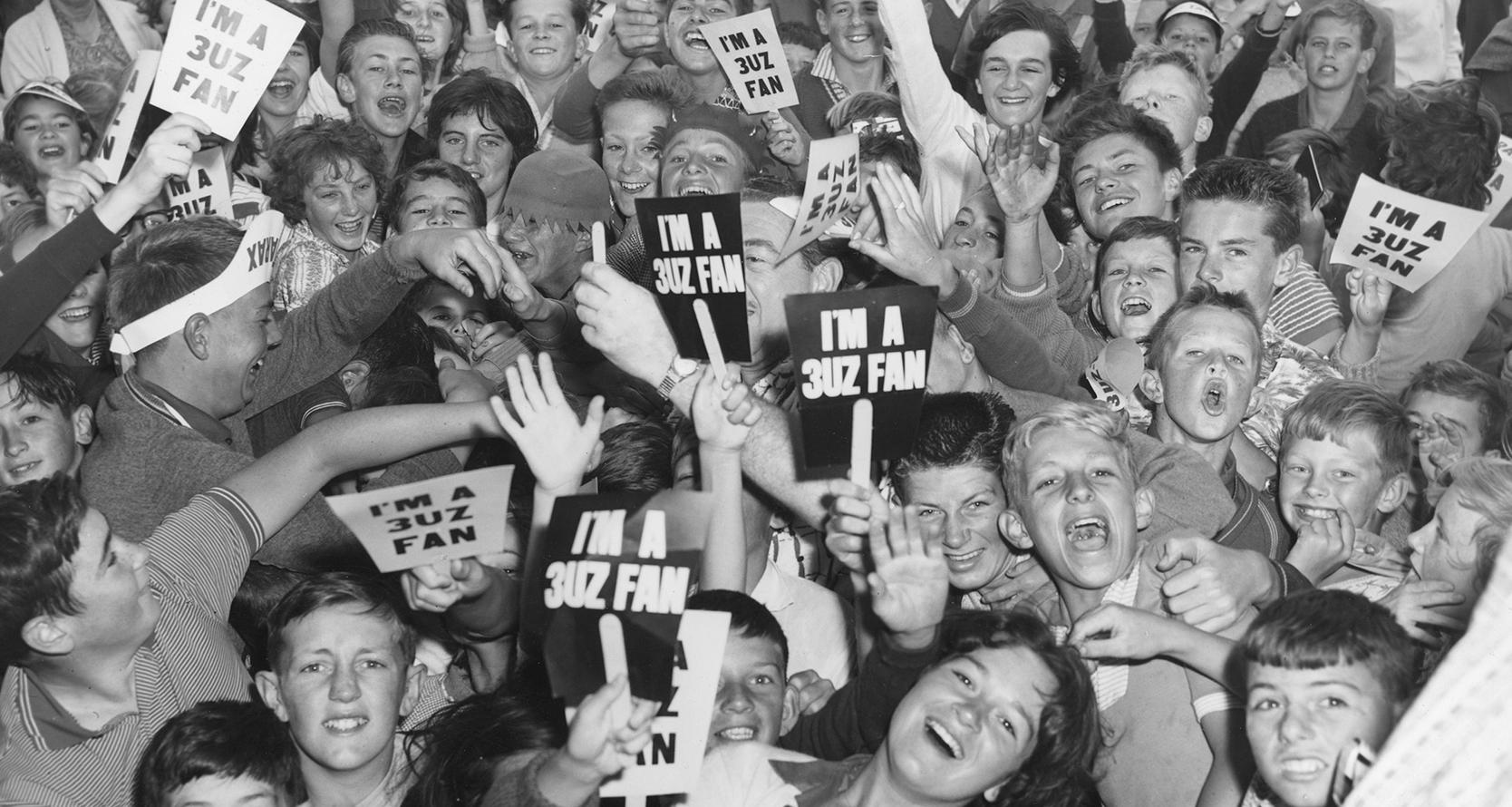 A group of teens cheering and holding signs that say 'I'm a 3UZ fan'