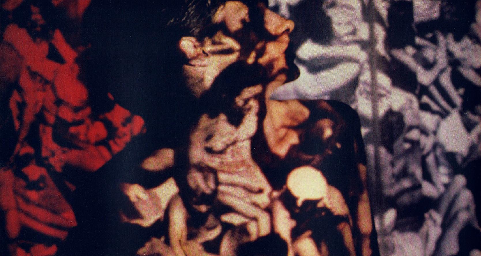 A person stands in front of a coloured screen projection showing a group of people sitting closely together in a crowd