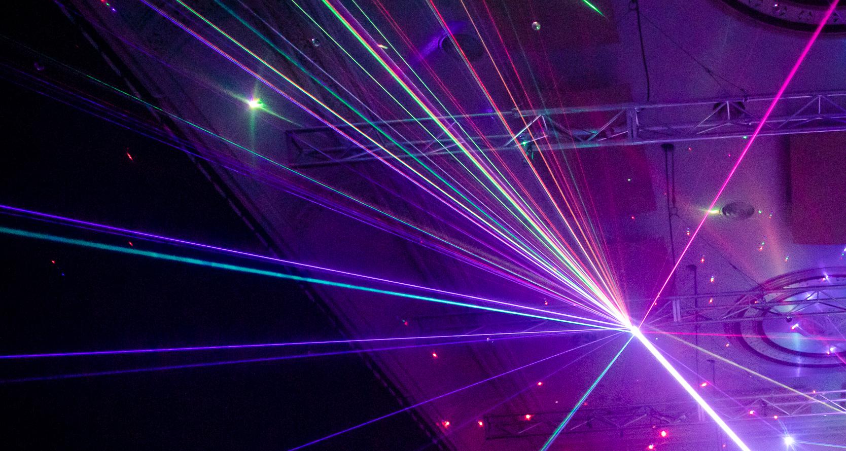 Beams of pink and purple lasers extending outwards from a central point on a gallery ceiling in the Constellations exhibition