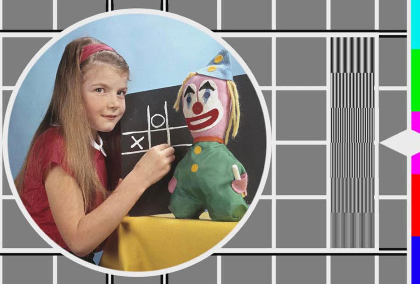 A colour TV test pattern with an inset image of a young girl in front of a chalkboard with a toy clown beside her