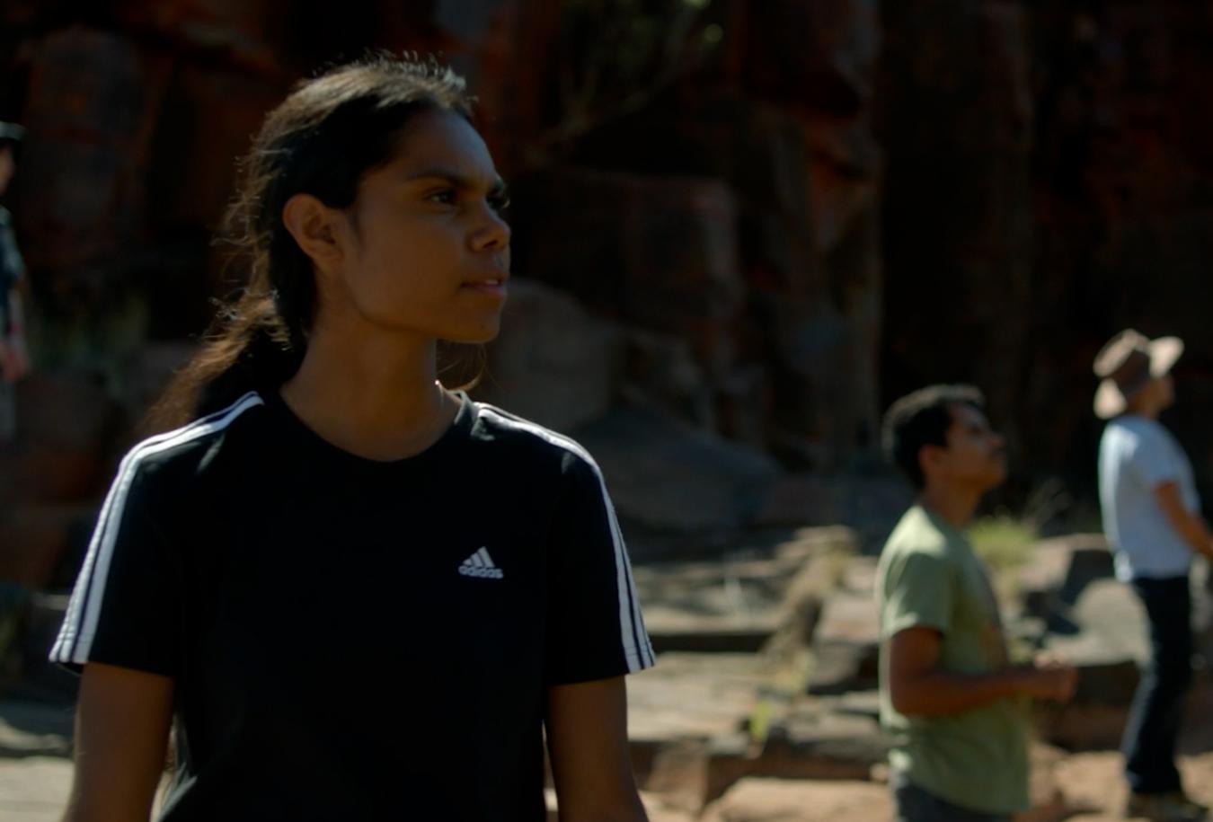 A young First Nations woman standing on a rocky surface in the outback
