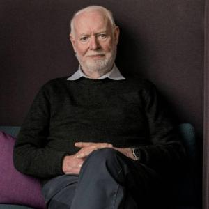 Film critic and author David Stratton seated on a sofa looking directly at the camera.