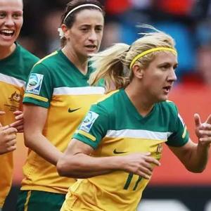Five players from the Australian Women's Soccer team running side by side, they are smiling and look to be celebrating scoring a goal.