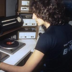 Radio and TV personality Lee Simon sitting in a radio studio in front of some turntables. He is turned slightly away from the camera.