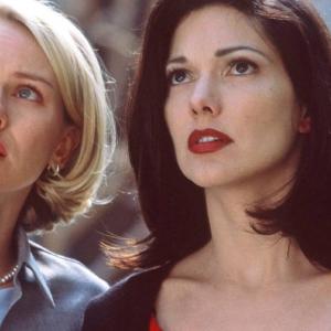 A blonde woman stands next to a woman with darker hair, both looking upwards with expectant expressions