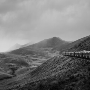 Black and white image of train running through mountains 