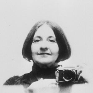 Experimental filmmaker Corinne Cantrill holding up an analogue film camera and smiling