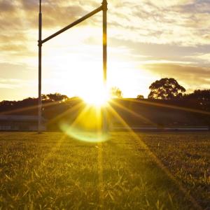 The rugby league goal posts on a football pitch are backlit by the setting sun