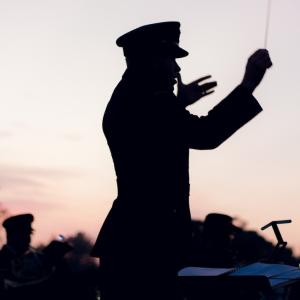 A silhouette of an orchestra conductor in military uniform waving his baton during a dawn service on Anzac Day