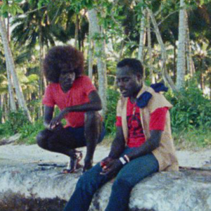 Two men in casual clothes sitting on a rock talking in the highlands of Papua New Guinea.