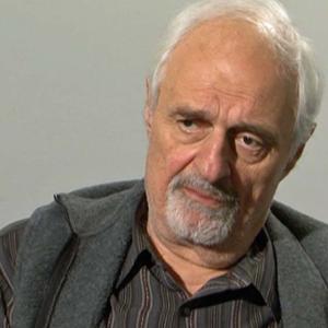 Ted Kotcheff in front of a grey background
