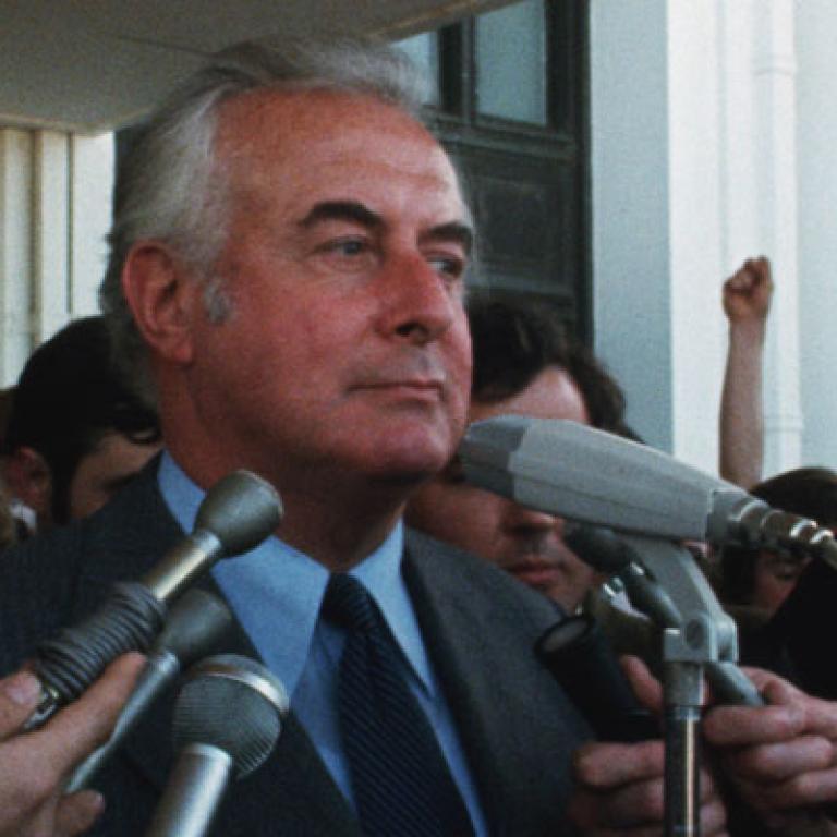 Gough Whitlam on the steps of Parliament House speaking into media microphones.