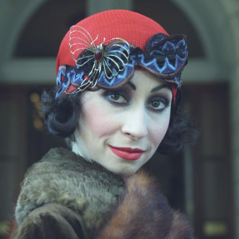 Close up of a woman dressed in a 1920s style hat and dramatic makeup, looking directly into the camera.