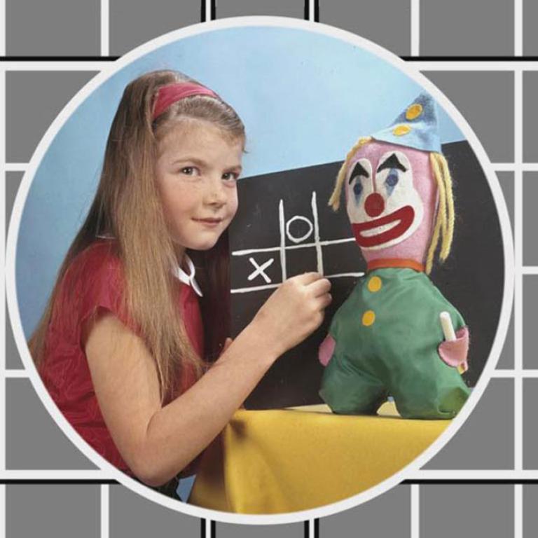A colour TV test pattern with an inset image of a young girl in front of a chalkboard with a toy clown beside her