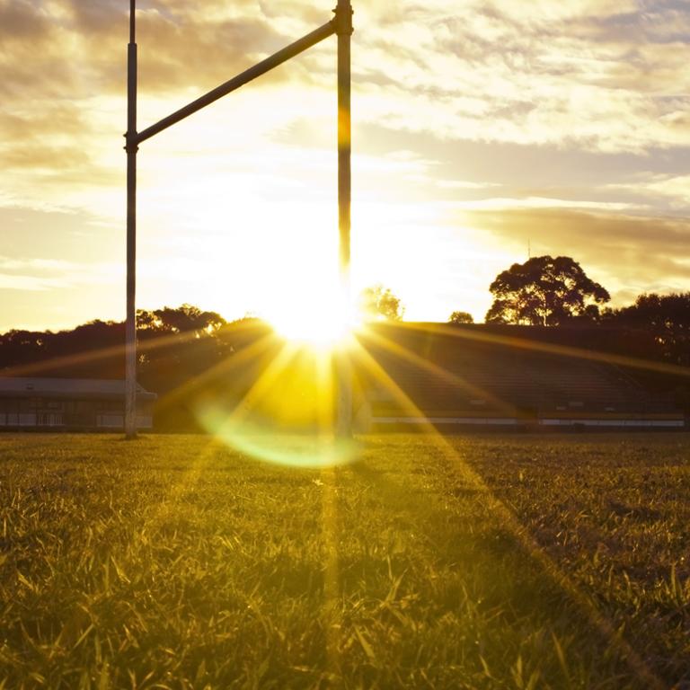 The rugby league goal posts on a football pitch are backlit by the setting sun