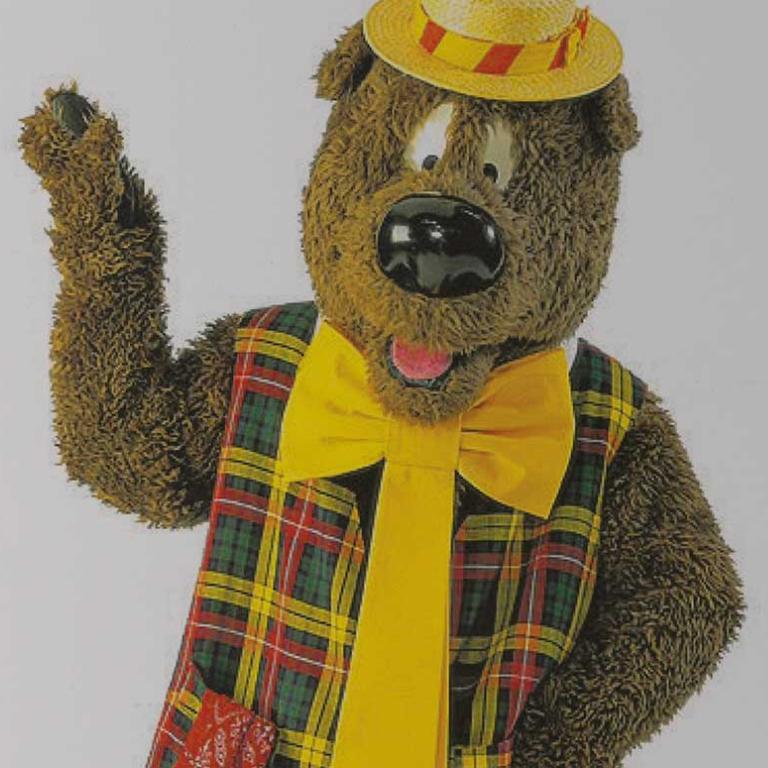 Upper body image of children's TV character Humphrey B. Bear wearing a plaid vest, yellow tie and boater hat.