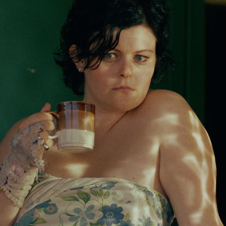 Genevieve Lemon holding a coffee mug and looking out the window in a still from the film Sweetie.
