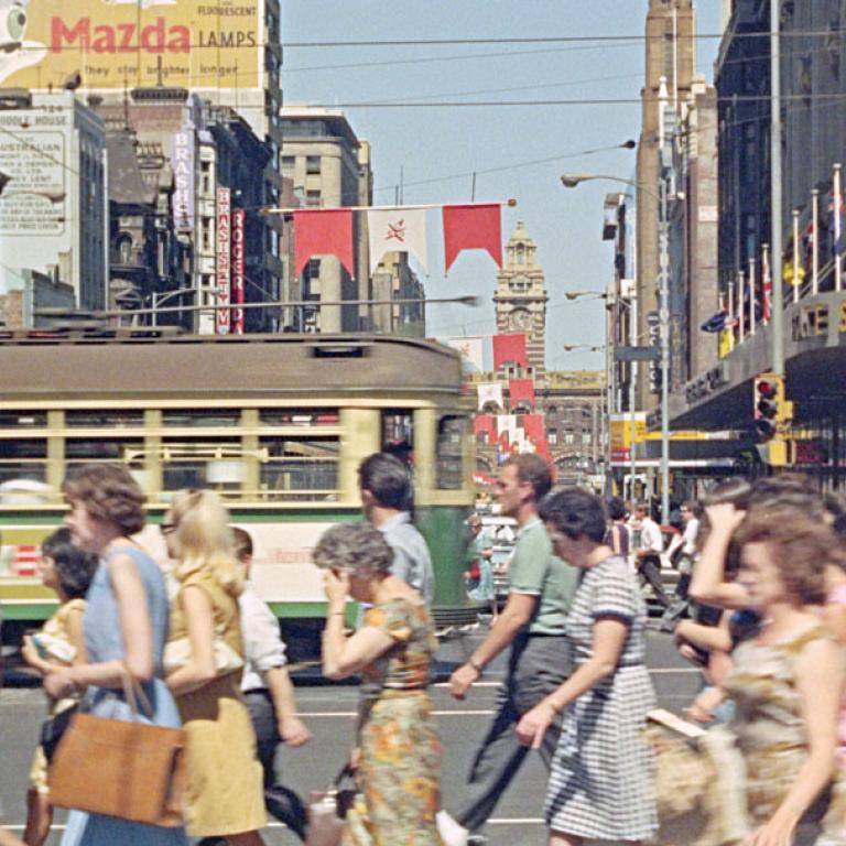 A busy street in Melbourne city with pedestrians and a tram going past.