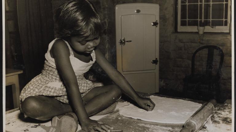 Production Still from Jedda: Young Jedda A small Aboriginal girl seated on a table playing.