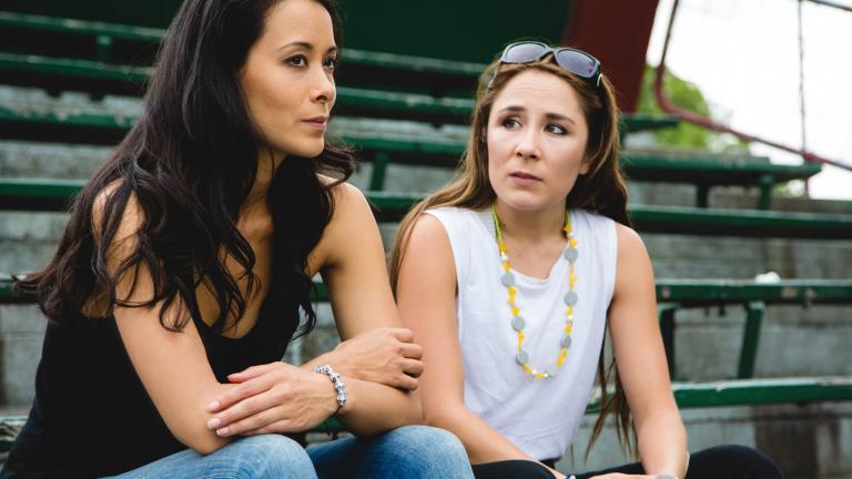 Two young women sitting in the stands of a local sporting ground.