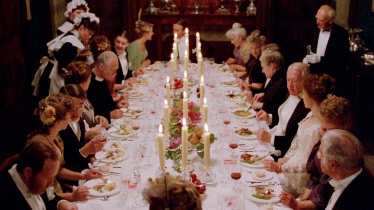 A large 1890s dinner party is in full swing as seated guests converse and eat while being served by maids and a butler in a scene from My Brilliant Career A large 1890s dinner party is in full swing as seated guests converse and eat while being served by maids and a butler in a scene from My Brilliant Career