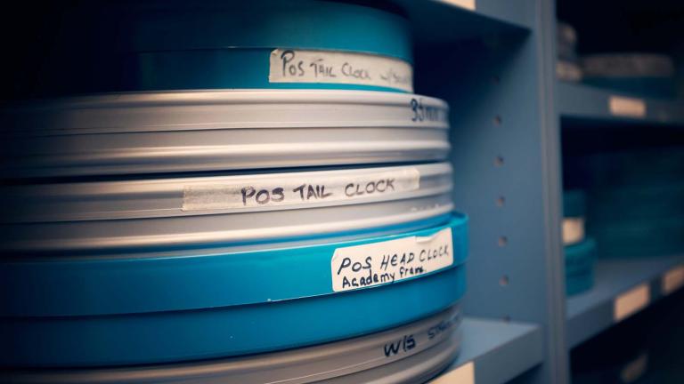 Blue and white film cans sit on a blue mental shelf