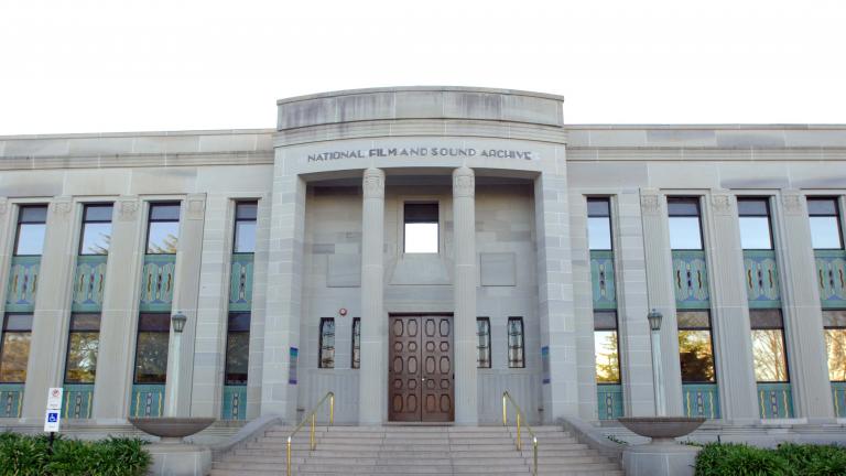 Art Deco NFSA building from front view, with blue sky in the background and flags flying atop of the building