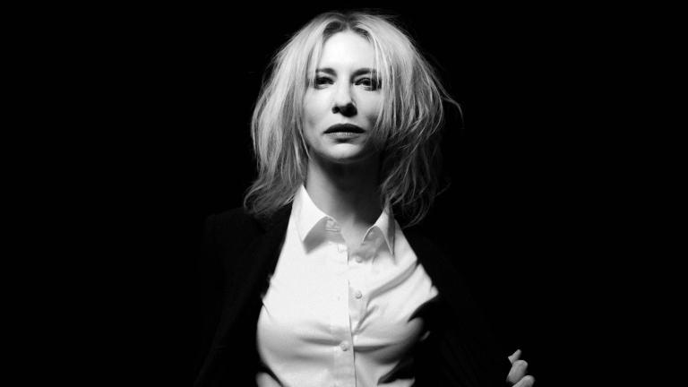 Black and which image of a woman pictured from the waist up wearing a black jacket and white collared shirt staring directly at camera