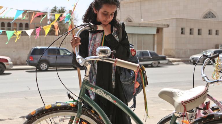 A young girl looking at a green bicycle.