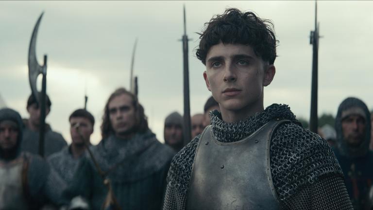 A young man wearing battle armour with an army standing behind him.