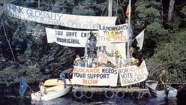 Demonstrators protest with banners on the side of a river