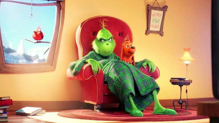 Animation still from the film The Grinch showing a grumpy-looking green cartoon character sitting on a lounge chair in a living room.
