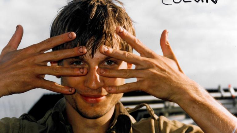 Head and shoulders shot of a young man holding his hands up in front of his face with his fingers spread out.