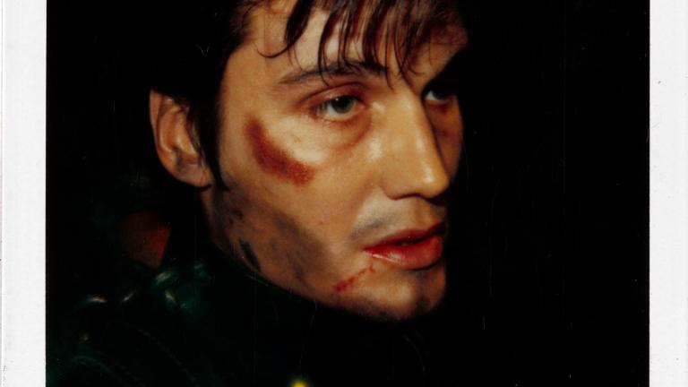 Close up of an actor's face in profile. He has make-up applied to make him look beaten and bruised.