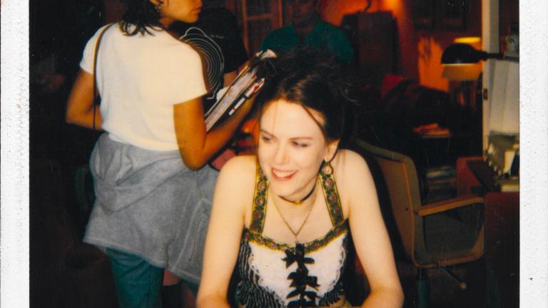 Actor Nicole Kidman seated and smiling, circa 1999. A woman stands behind her with her back towards the camera.