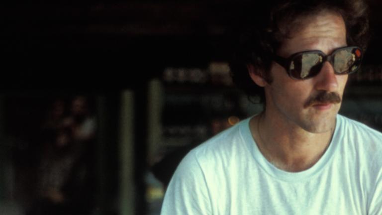 Head and shoulders shot of filmmaker Werner Herzog c1980. He is wearing a white t-shirt and sunglasses and looking off camera.