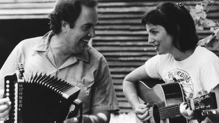 A man playing an according seated next to a woman playing guitar.