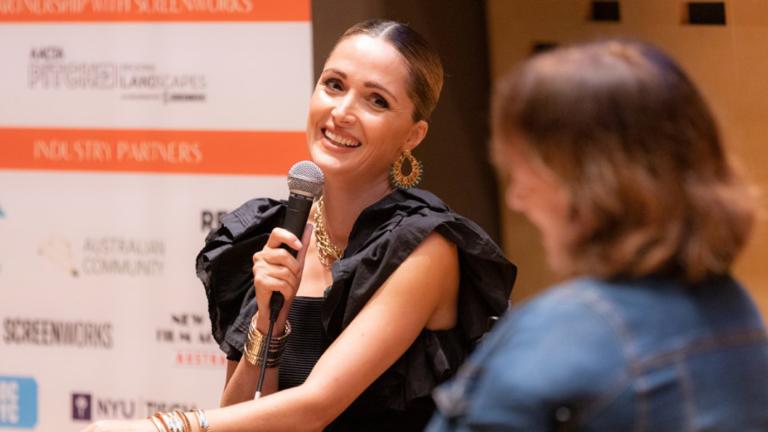 Rose Byrne holds a microphone at an onstage Q&A