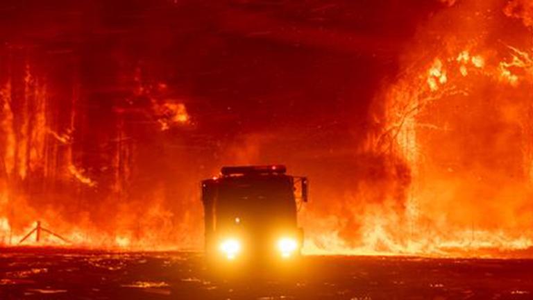 Silhouette of a fire truck surrounded by bushland that is on fire and glowing orange.