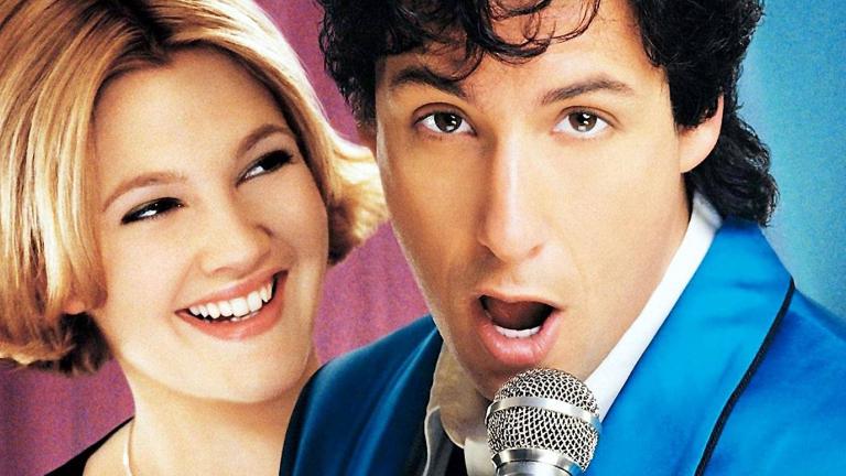 Close up of a young woman with short blonde hair (Drew Barrymore) smiling and looking at a man (Adam Sandler) singing into a microphone in a promotional shot for the film The Wedding Singer.